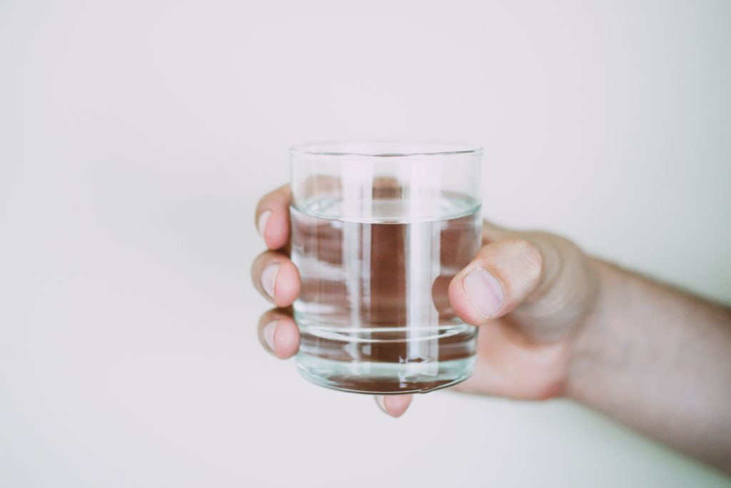 A hand holding a glass of water, symbolizing how water and proper hydration helps in weight loss