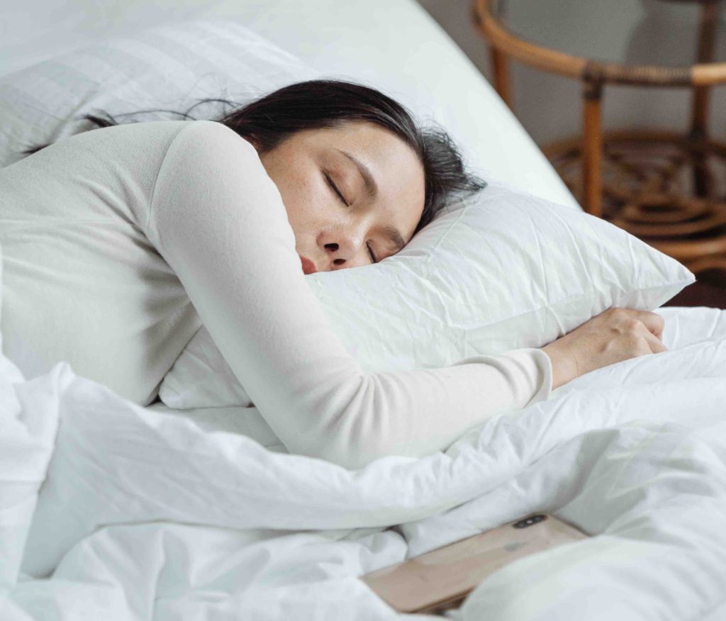 A woman holding a pillow and sleeping to symbolize how sleep is essential for health and weight loss